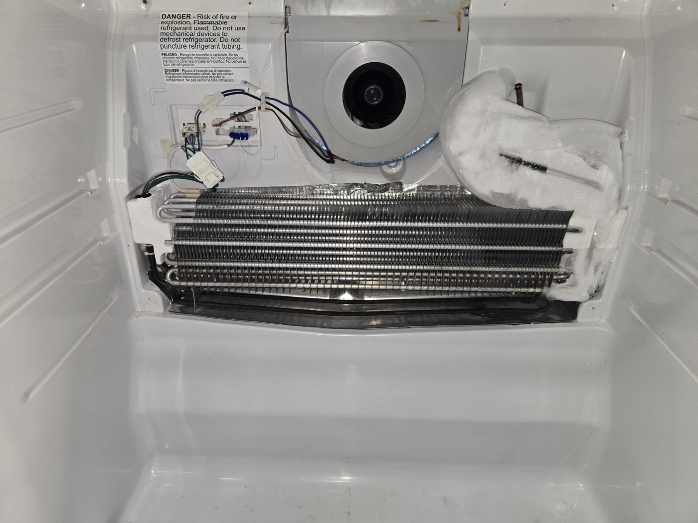 Evaporator coils exposed behind a refrigerator freezer panel